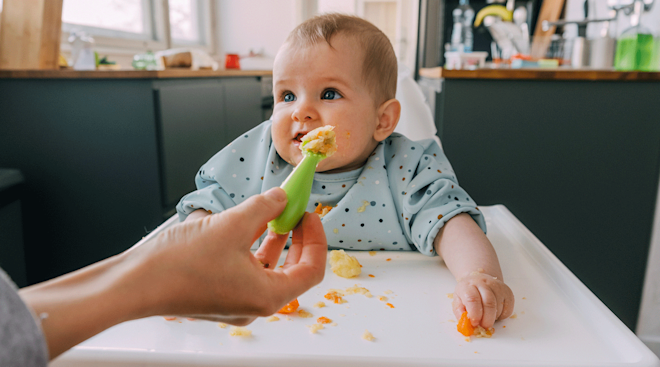 mom feeding baby food in high chair at home