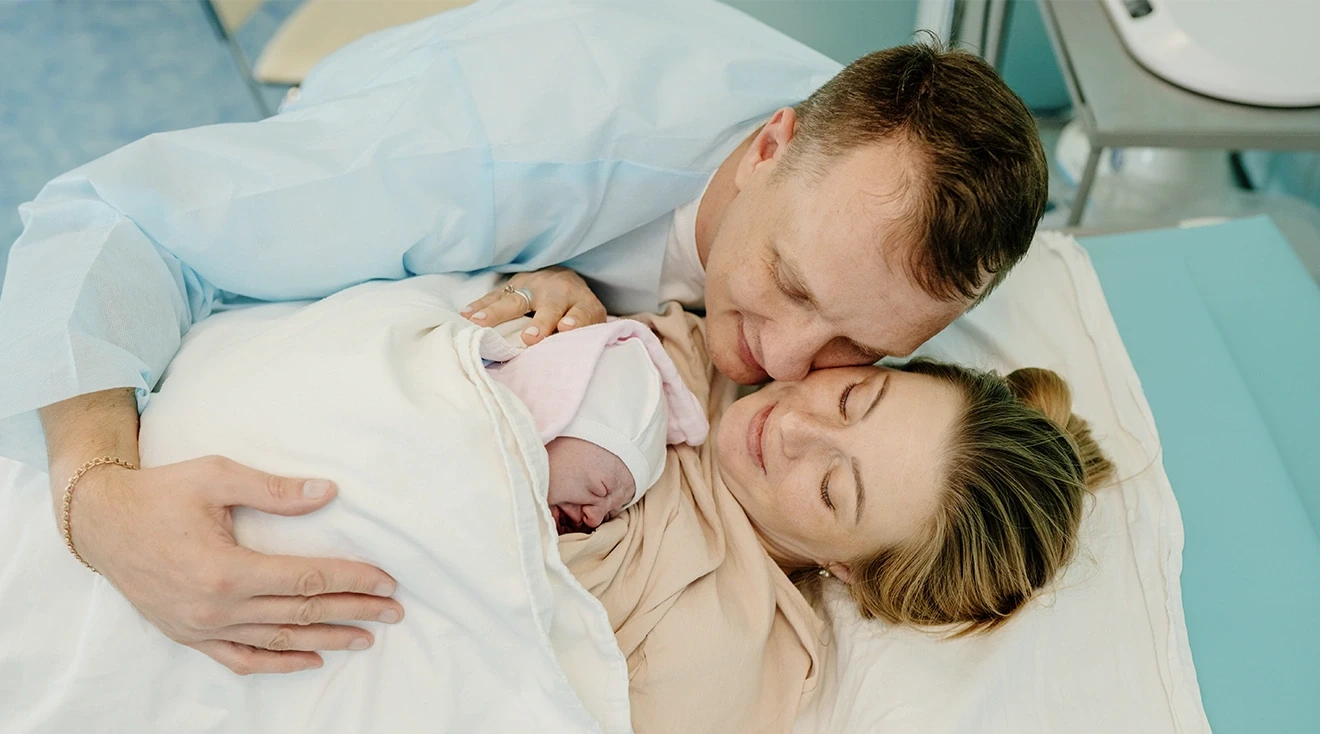 man hugging wife and newborn baby in the hospital delivery room