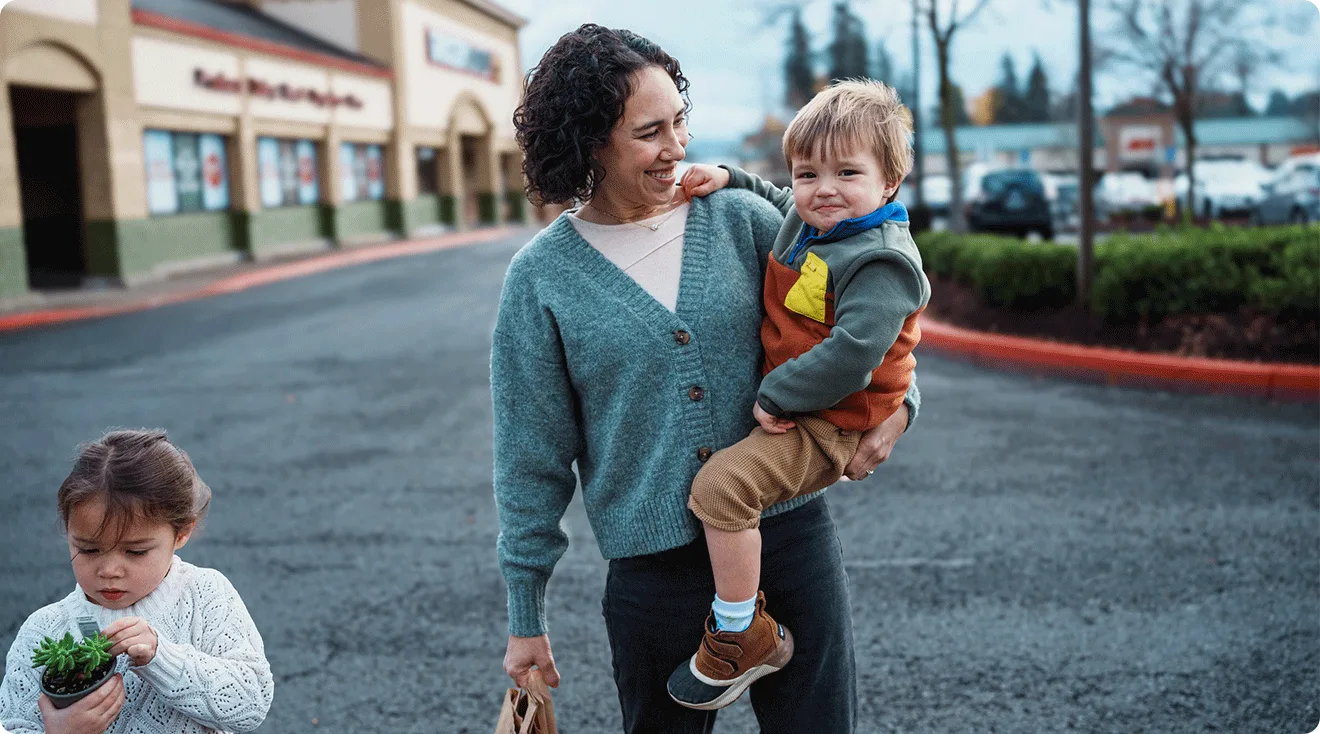 mother holding toddler while walking in grocery store parking lot