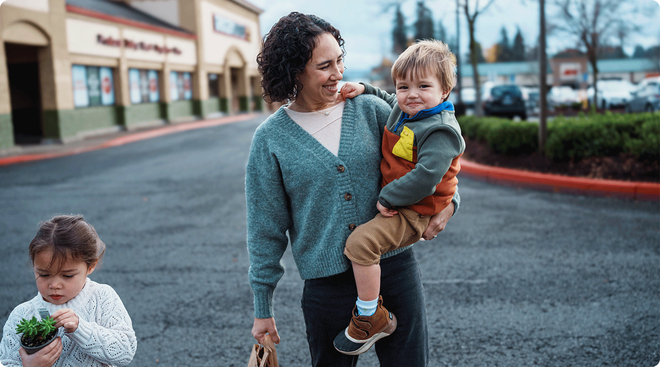 mother holding toddler while walking in grocery store parking lot