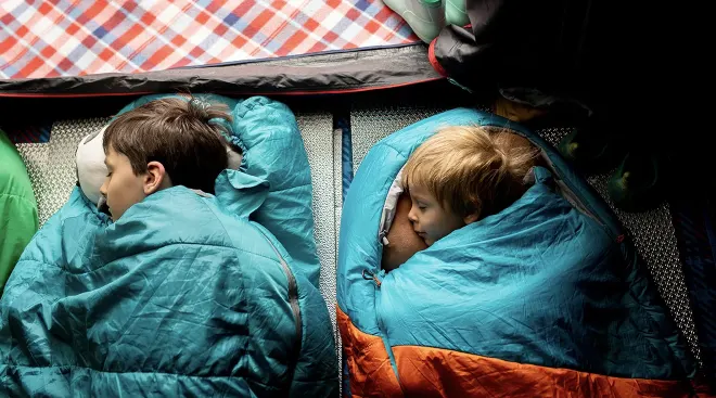 two children in sleeping bags in a tent while camping