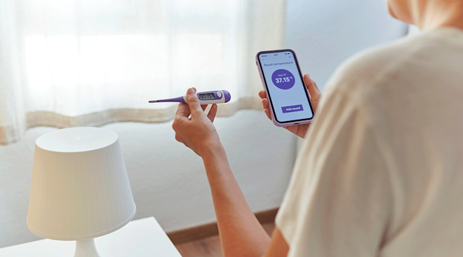 woman checking basal body temperature with thermometer and phone app