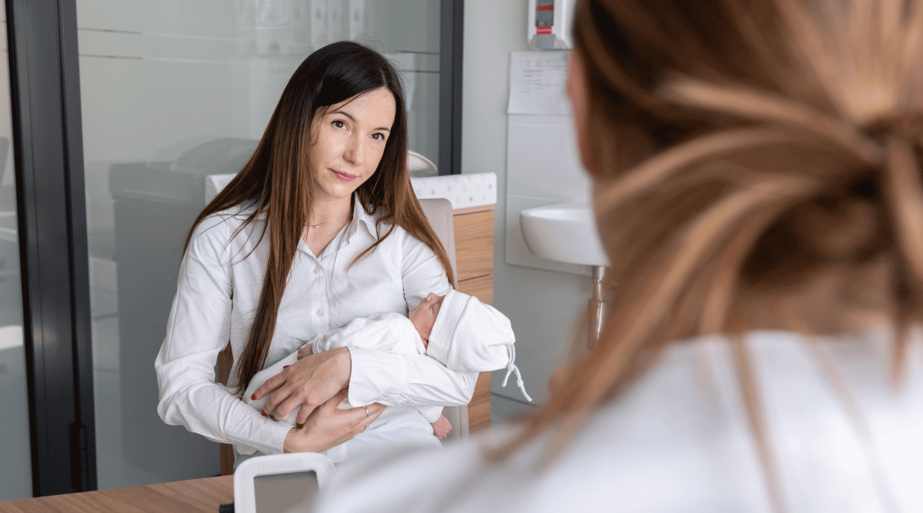 doctor talking to mom holding newborn baby during baby's first check up