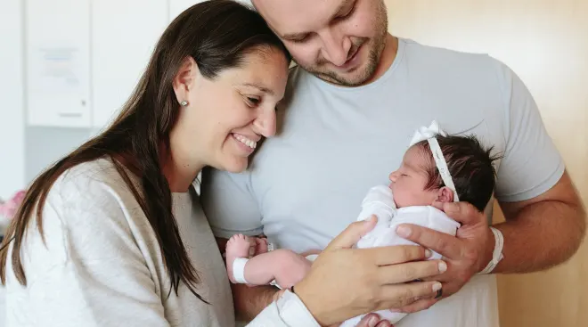 smiling parents holding their newborn baby at home