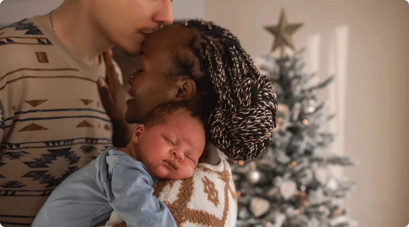 parents with newborn baby in front of christmas tree at home