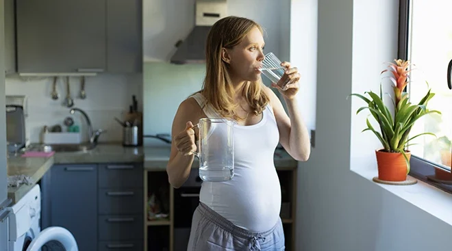 pregnant woman drinking water in kitchen at home