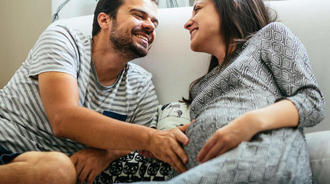 Pregnant woman and her partner together on the couch laughing