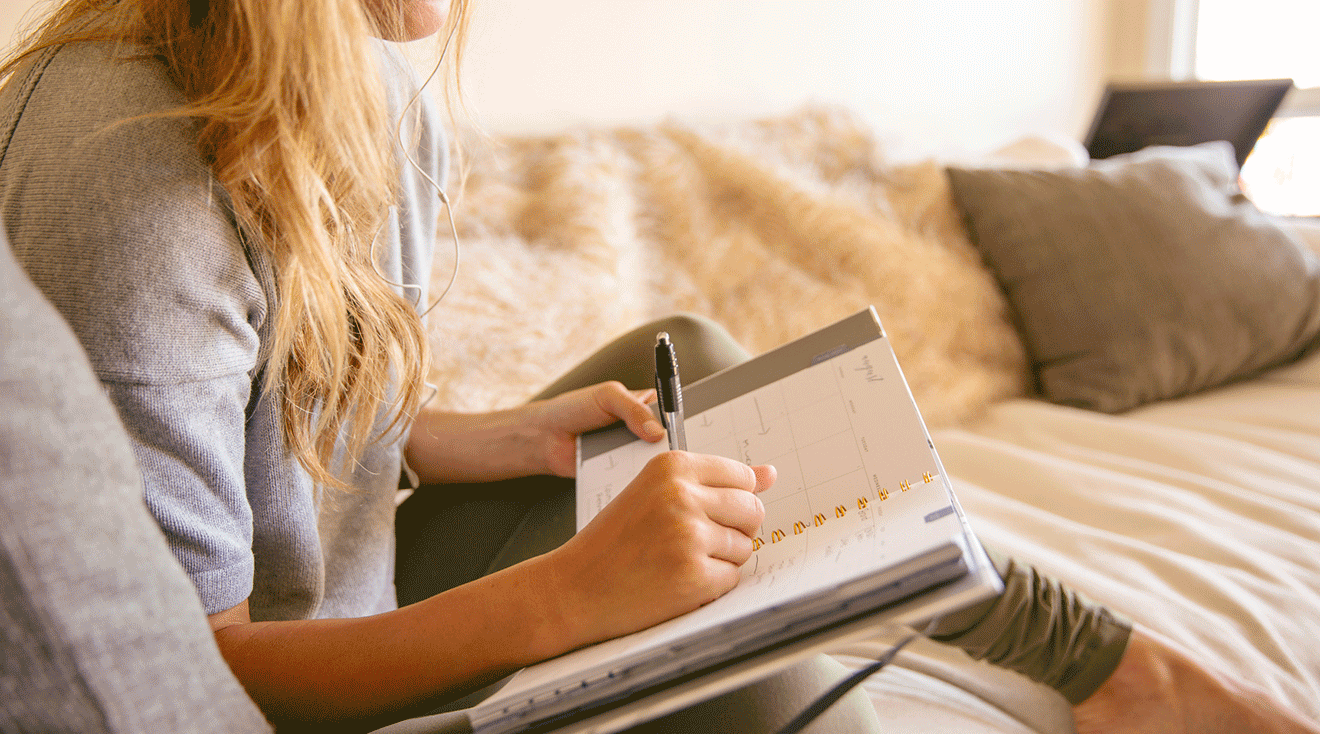 young woman writing in planner notebook to track ovulation and menstruation