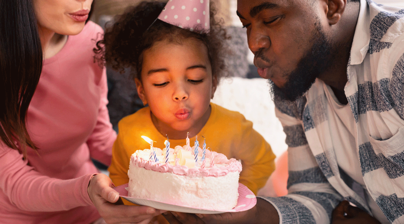 parents blowing out birthday candles with young daughter