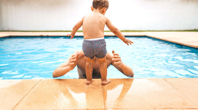 toddler about to jump into his dad's arms in the pool