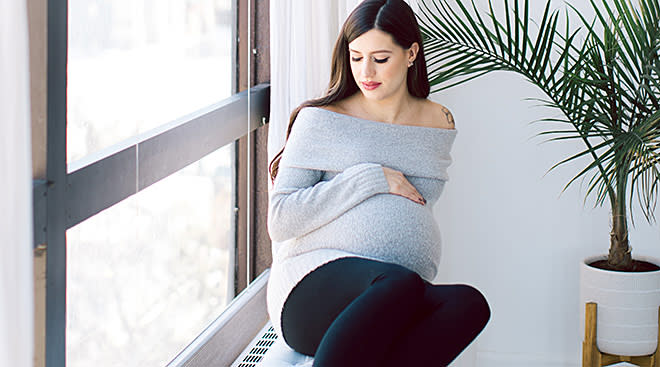pregnant woman sitting on couch by window at home