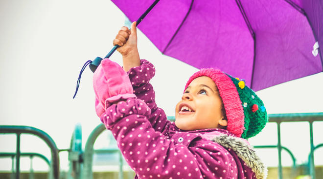 happy little girl looking up and holding purple umbrella