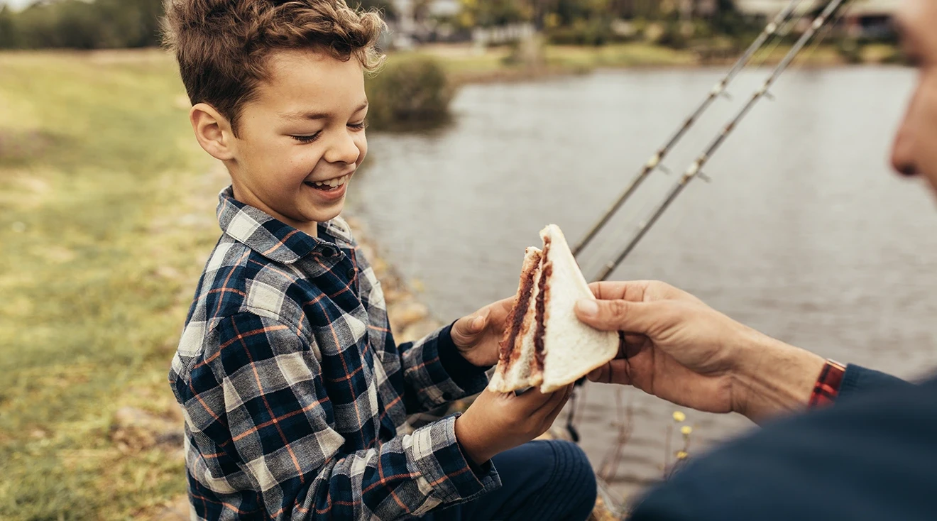 father handing his son a peanut butter and jelly sandwich at the park