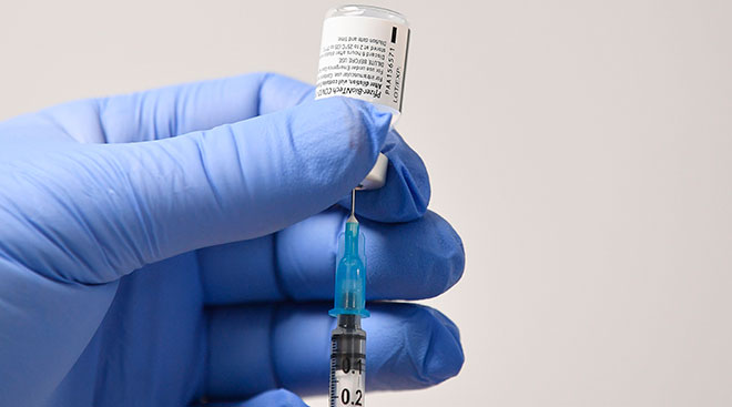 close up of doctor hands with blue gloves holding covid vaccine vial and needle