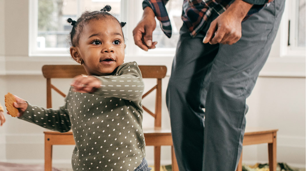 cute toddler girl dancing at home with dad in the background