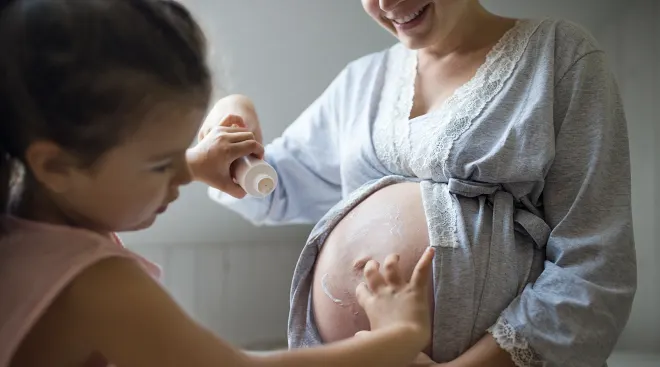 little girl helping mother apply lotion to pregnant belly