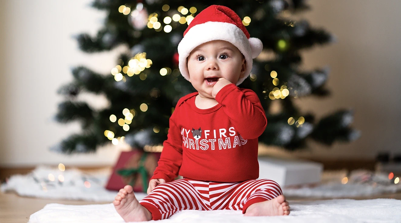 baby wearing a christmas outfit in front of christmas tree at home