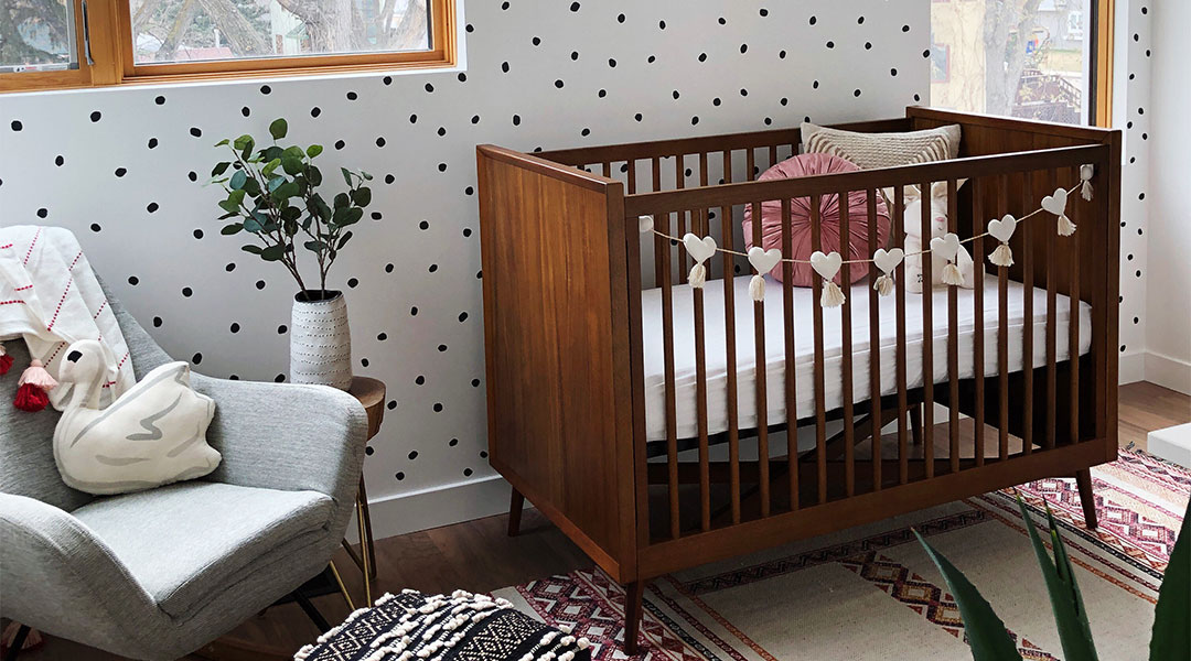 interior shot of baby girl nursery with medium wood crib and polka dot accent wall
