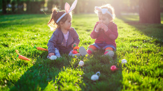 Two toddler girls playing with easter crafts outside on the grass