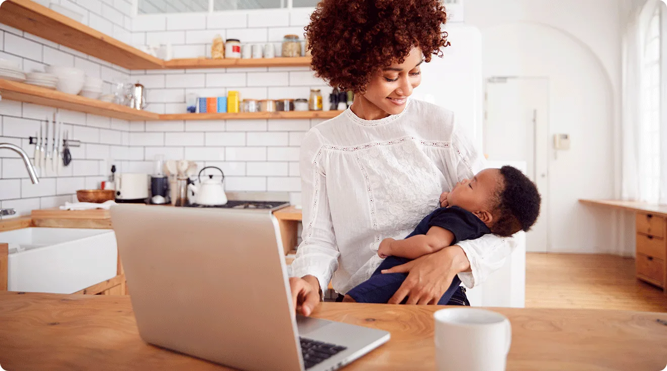 mom holding baby while using laptop at home