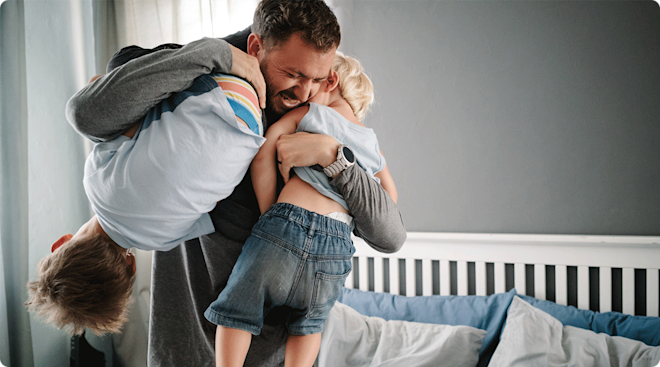 A smiling dad rough housing with two young sons at home.