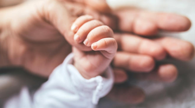 newborn is kissed causing herpes, parent holding newborn's hand