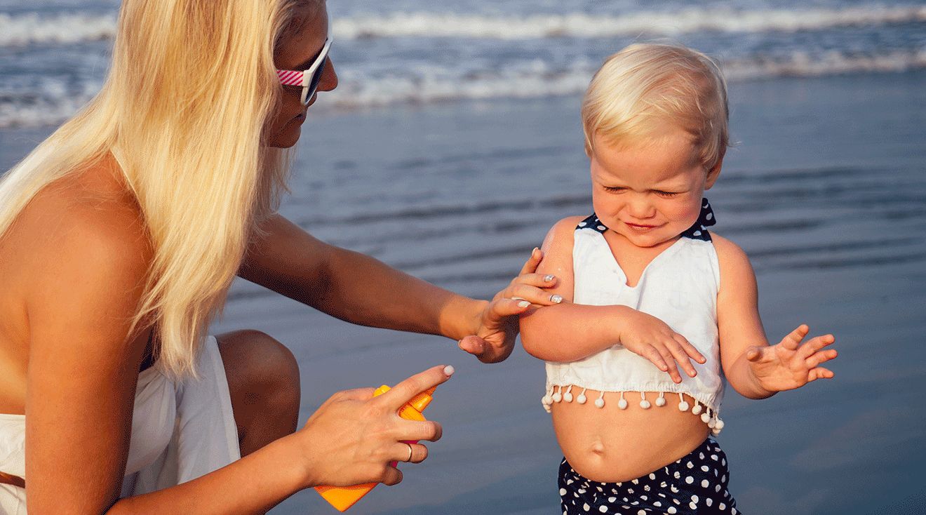 mom putting sunscreen on toddler at the beach