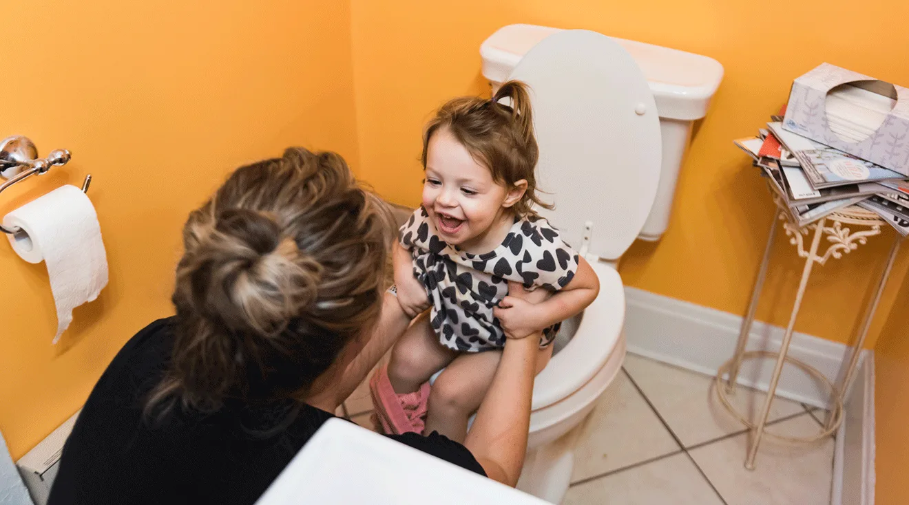 mom helping toddler on the toilet for potty training