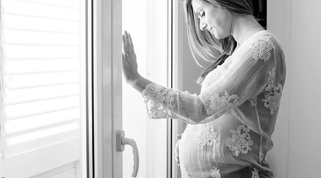 pregnant woman stand by window and looks down while touching her bump