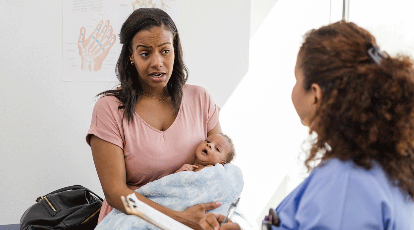 postpartum mother talking to doctor while holding newborn baby in doctor's office