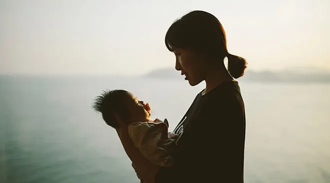 mother looking at her baby with the ocean in the background