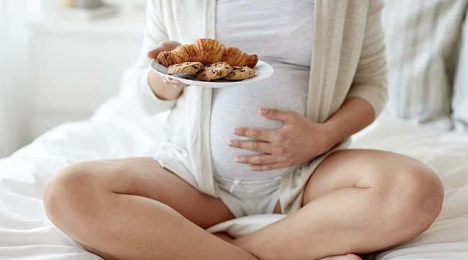pregnant woman holding a plate of cookies and croissants