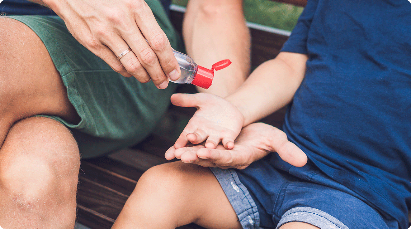 dad giving toddler hand sanitizer on park bench