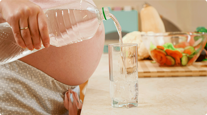 pregnant woman pouring water from plastic water bottle