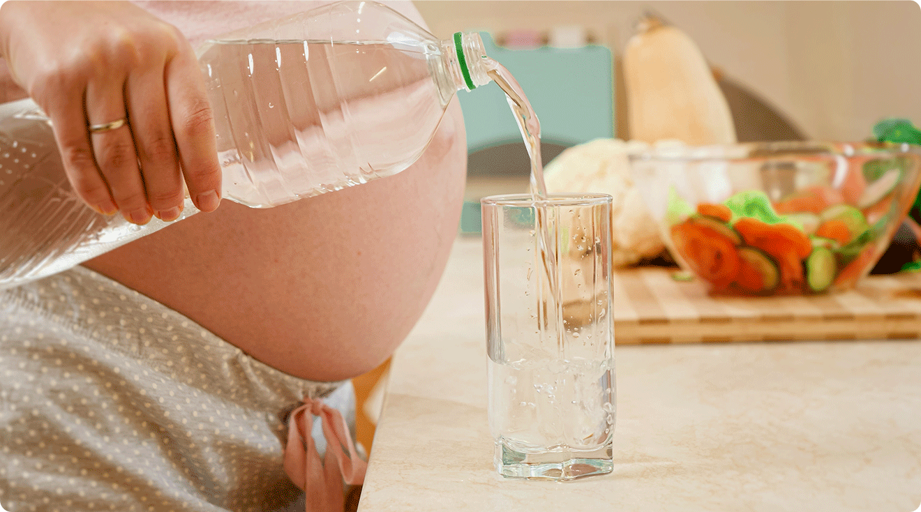 pregnant woman pouring water from plastic water bottle