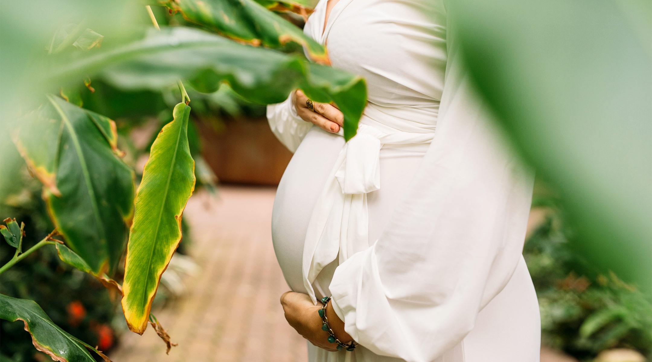 serious pregnant woman standing in tropical greenhouse