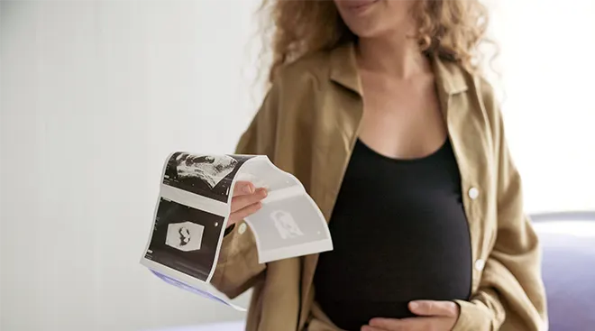 pregnant woman holding ultrasound pictures at the doctor's office