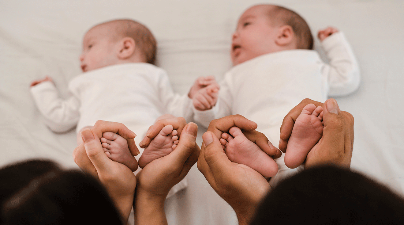 parents holding newborn twins feet at home