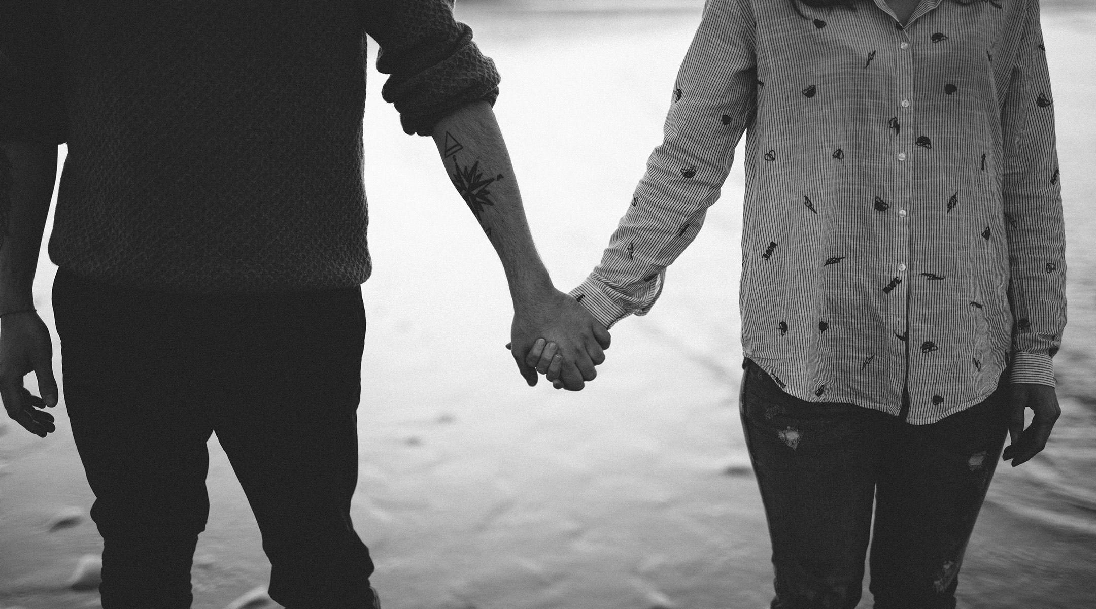 black and white image of serious couple holding hands near water