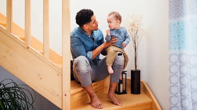 father talking to toddler while sitting on stairs at home