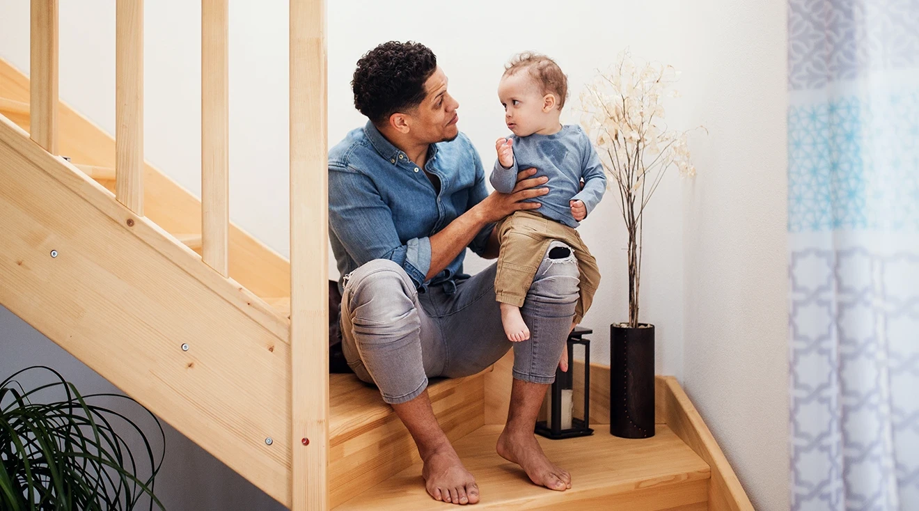 father talking to toddler while sitting on stairs at home