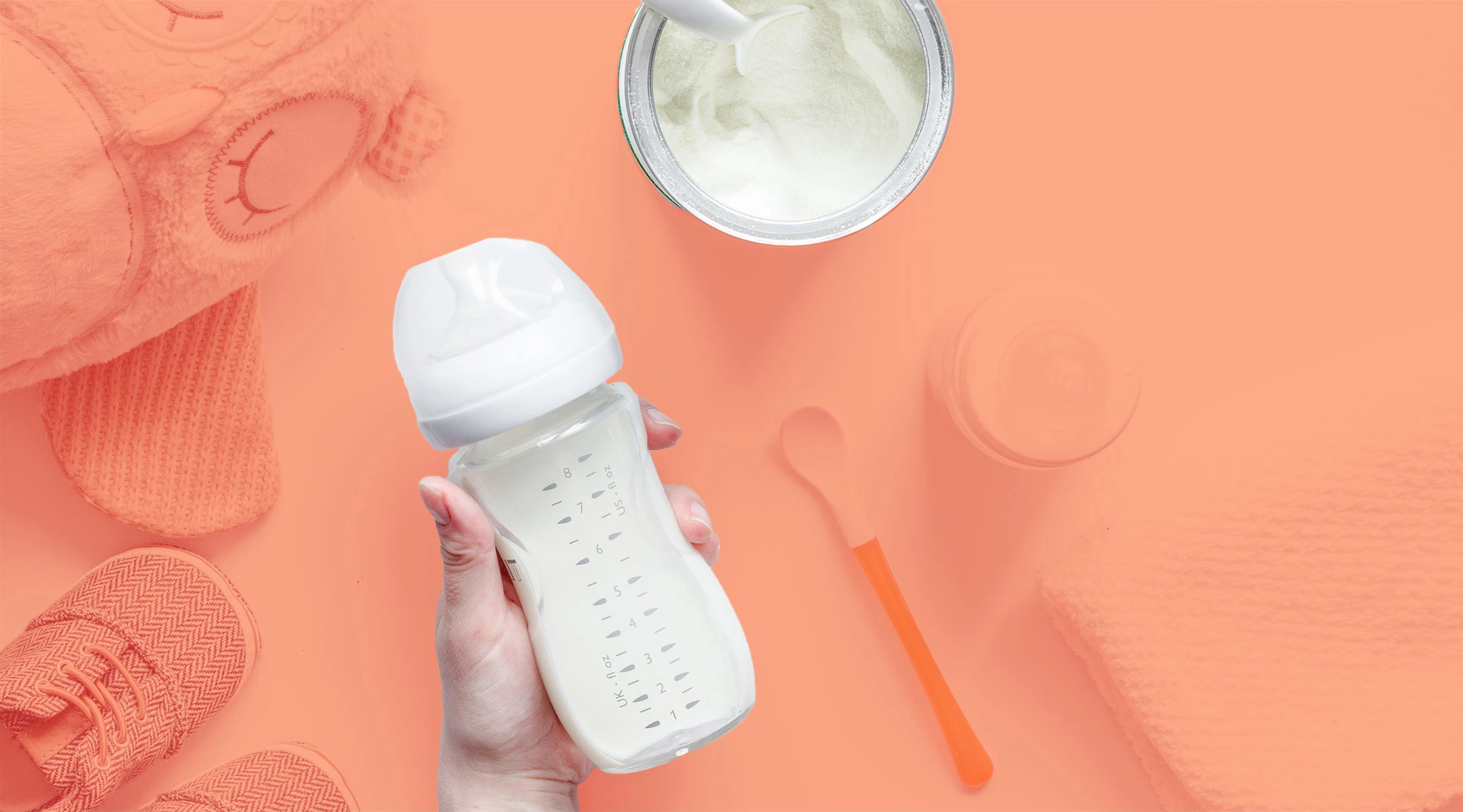 hand holding formula filled bottle on orange tinted background