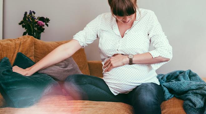 pregnant woman in pain holding stomach on couch 