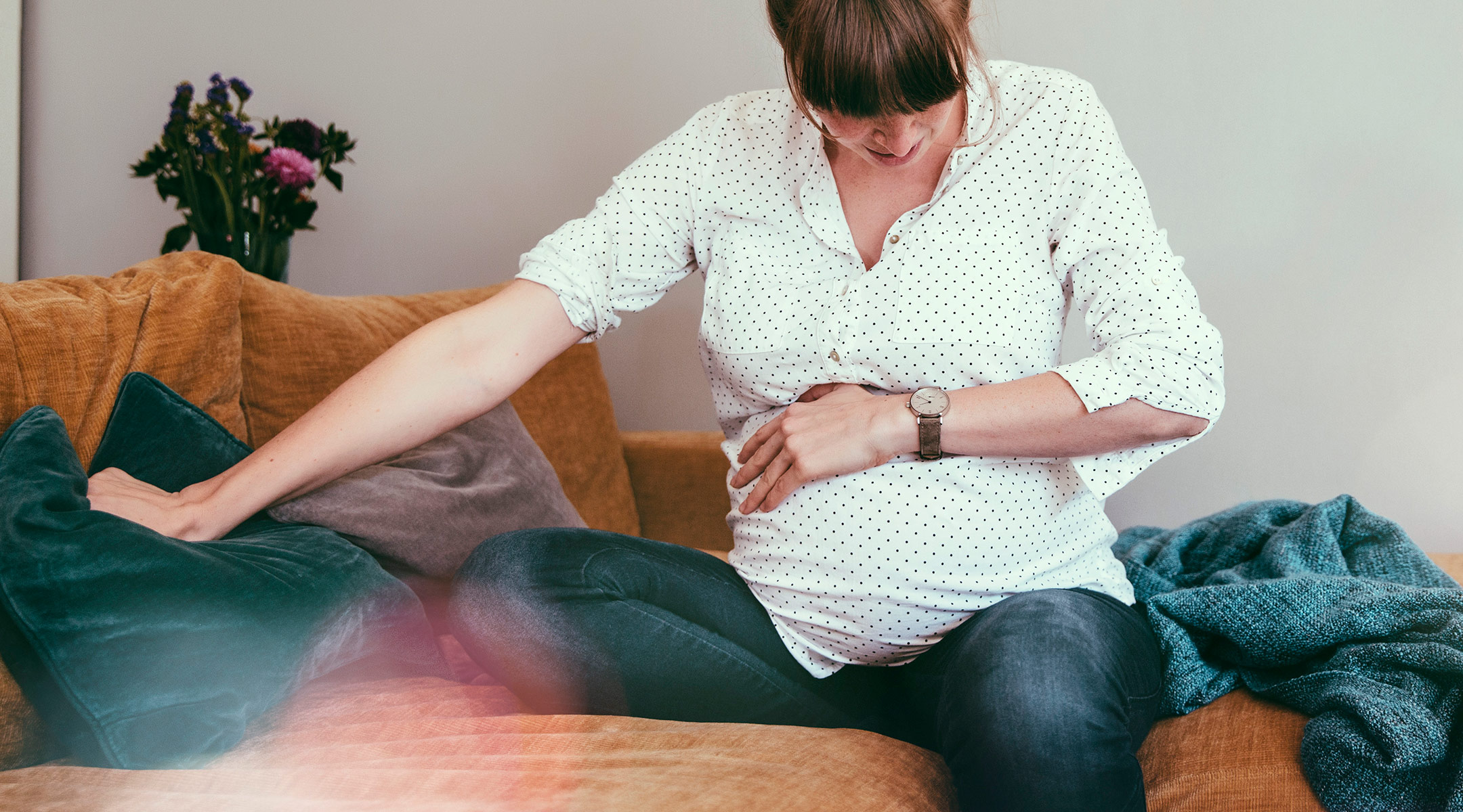 pregnant woman in pain holding stomach on couch 