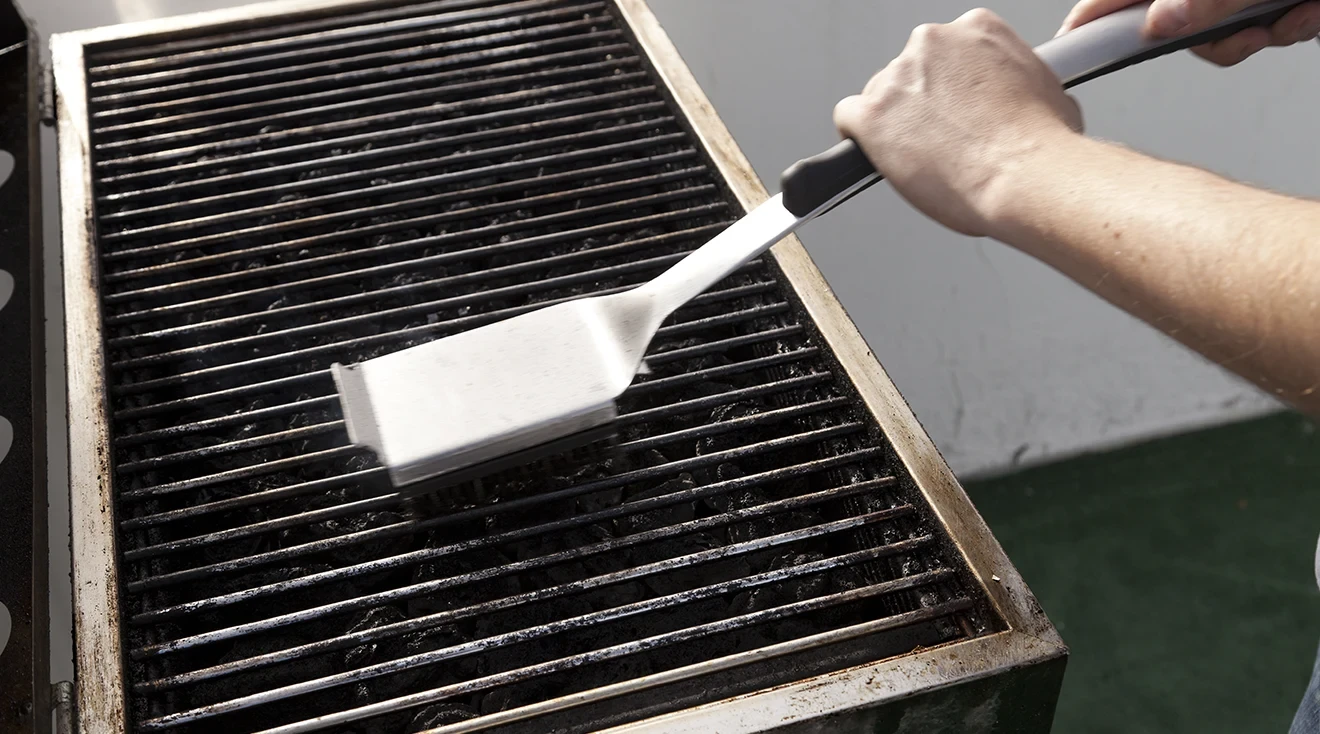 person cleaning a barbecue grill with a wire brush