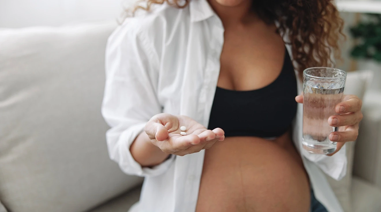 pregnant woman holding glass of water and two white pills