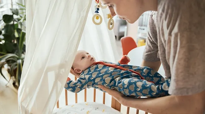 mother putting baby in crib