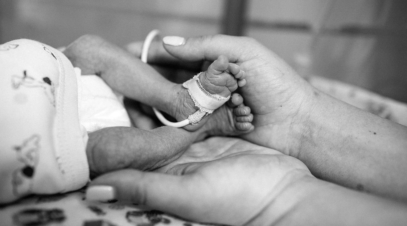 mother holding premature baby's feet in the NICU
