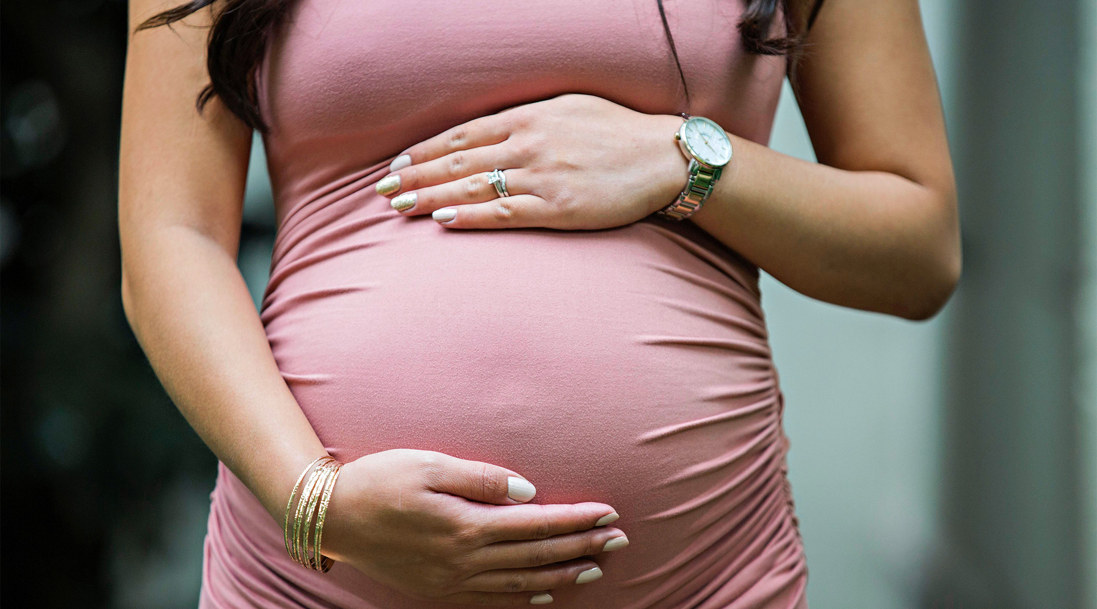 pregnant woman with her hands on her belly wearing a pink dress