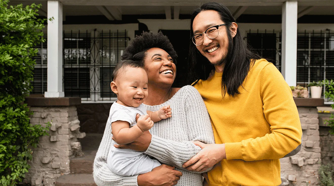 family with baby standing outside of home